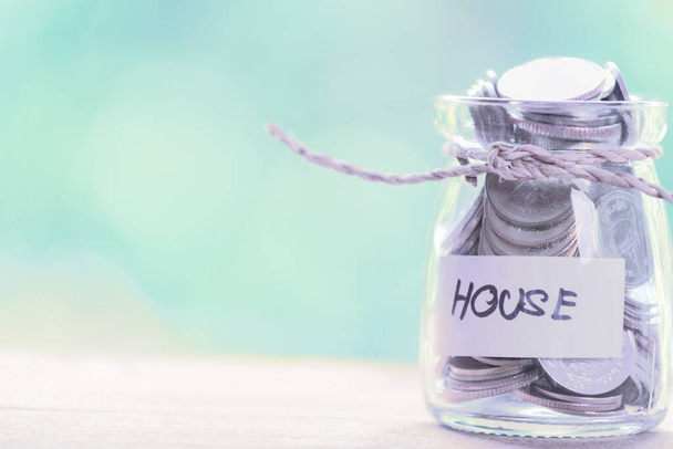 Saving money for house,coins in glass jar with quote house on wood table with pastel blurred background - Φωτογραφία, εικόνα