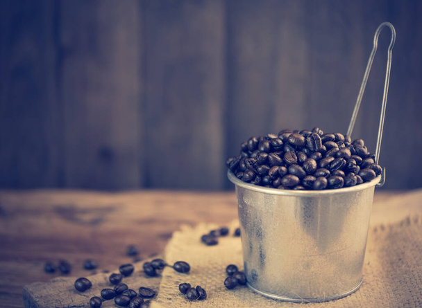Pražená kávová zrna v pozinkované hrnci přes grunge dřevěné pozadí - Fotografie, Obrázek