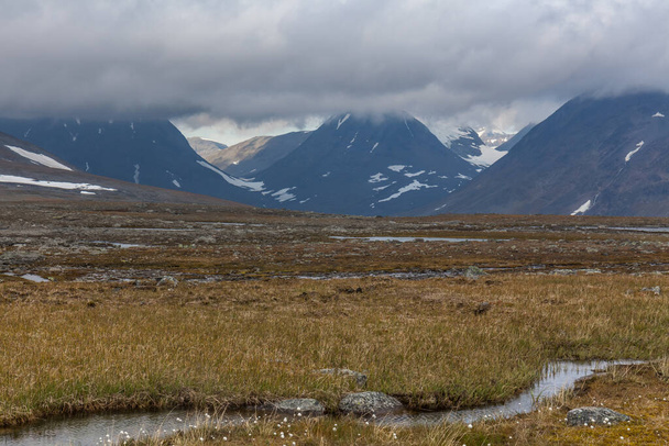 Beautiful wild nature of Sarek national park in Sweden Lapland with snow capped mountain peaks, river and lake, birch and spruce tree forest. Early autumn colors in stormy weather. selective focus - Fotó, kép