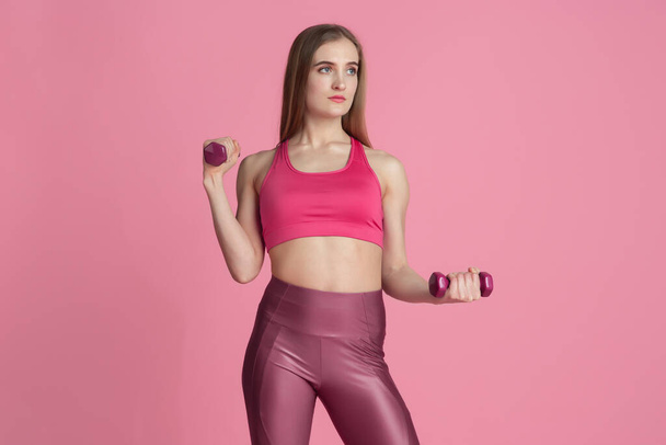 Beautiful young female athlete practicing on pink studio background, monochrome portrait - Fotó, kép