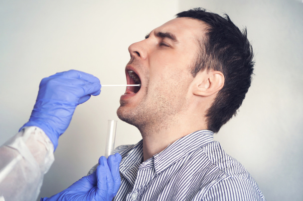 DNA test. Dokter doet Coronavirus covid 19 test voor mannelijke patiënt. Een speekselmonster nemen van een man. Verzameling van slijm uit de keel voor onderzoek in het laboratorium. - Foto, afbeelding