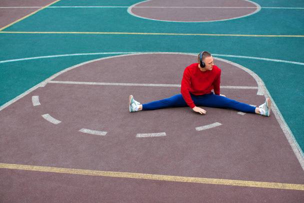 Un joven estira los músculos de sus piernas después de entrenar en el campo de deportes
. - Foto, imagen
