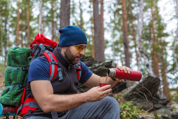Samec turisty nalévá čaj z termosky během zastávky v lese. - Fotografie, Obrázek