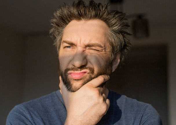 Смешной человек после пробуждения царапает бороду, глядя на утреннее солнце
. - Фото, изображение