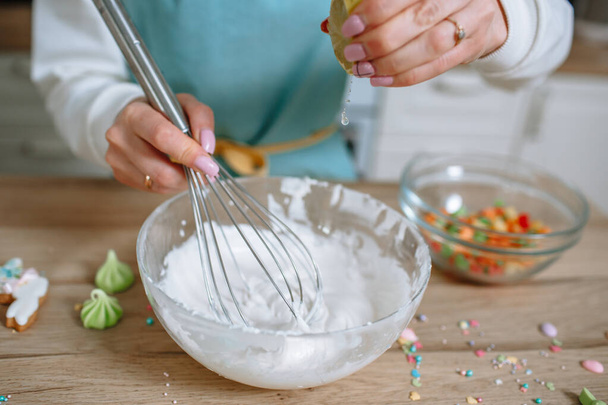 The smiling girl cook whips up the icing for the Easter cake with a whisk and squeezes a lemon into it - Photo, image