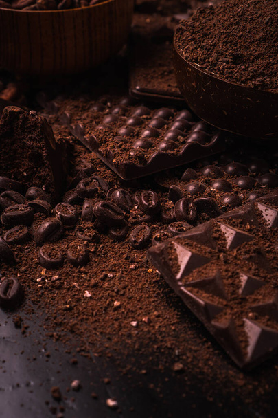 Cocoa beans, cocoa powder, cocoa butter, chocolate bar and chocolate sauce, chocolate bar in a wooden bowl on a dark background place for text - Foto, afbeelding