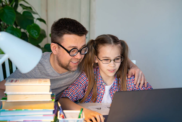 papa in bril helpt dochter lessen op laptop - Foto, afbeelding