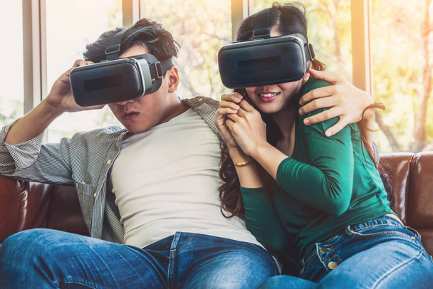 Happy couple watching video in virtual reality VR headset in living room at home. Multimedia movie and entertainment concept. - Φωτογραφία, εικόνα