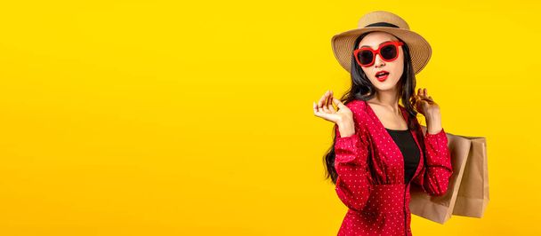 Banner einer asiatischen trendigen Shopaholic Frau, die sich über neue Einkäufe oder Verkäufe aufregt, Einkaufstüten in der Hand hält und nach Kopierraum auf gelbem Hintergrund sucht. Glückliche asiatische Kundin trägt Einkaufstüten. - Foto, Bild