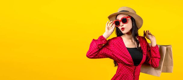 Banner trendiger Shopaholic Frau, die sich über neue Einkäufe oder Verkäufe aufregt, Einkaufstüten in der Hand hält und nach Kopierraum auf gelbem Hintergrund sucht. Glücklich schöne Asiatin trägt Einkaufstüten. - Foto, Bild