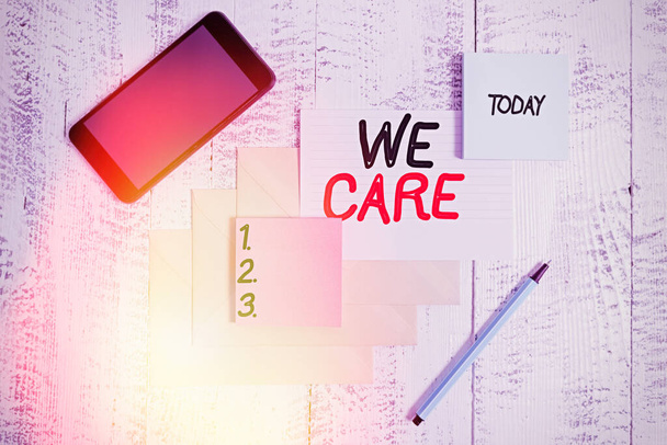Word writing text We Care. Business concept for Cherishing someones life Giving care and providing their needs Envelopes marker ruled paper smartphone sheet note pads wooden background. - Photo, Image