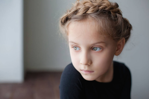 Een groot portret van een klein meisje op de vensterbank en triest. - Foto, afbeelding