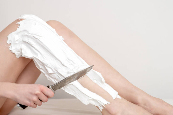 Hand of woman shaves her leg by a knife smeared with shaving foam on white background. Depilation or epilation concept. - Photo, Image