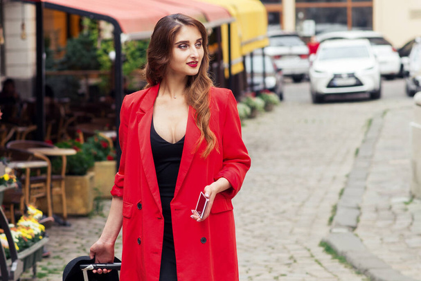 Ταξιδεύοντας επιχειρηματίας φορώντας κόκκινο μανδύα περπατά στο δρόμο της πόλης. - Φωτογραφία, εικόνα