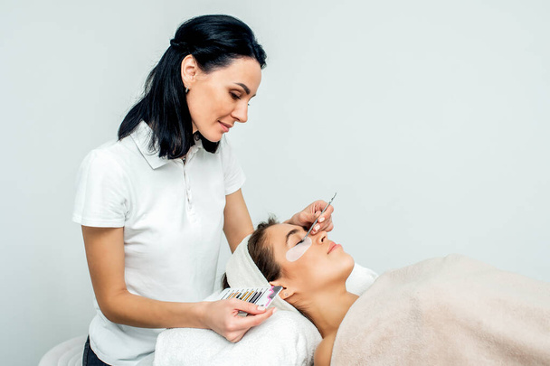Kosmetička pracující během prodlužování řas s pacientem na bílém pozadí s kopírovacím prostorem. - Fotografie, Obrázek