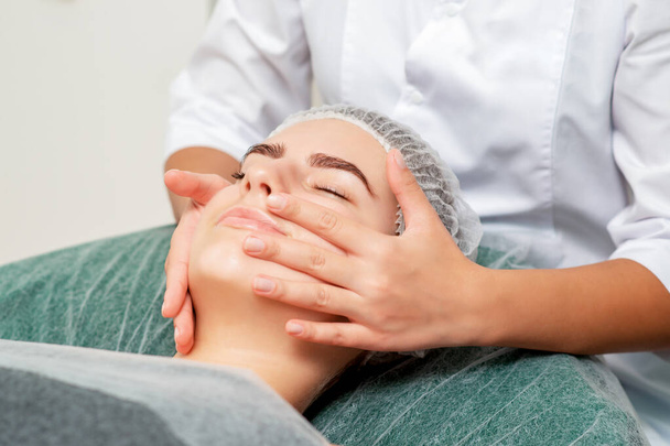 Massage de la tête de jeune femme par un cosmétologue au salon de beauté
. - Photo, image