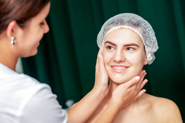Kosmetikerin berührt Gesichtshaut einer jungen Frau. - Foto, Bild