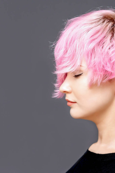 Femme avec coiffure rose se tient avec les yeux fermés vue latérale sur fond gris avec espace de copie
. - Photo, image