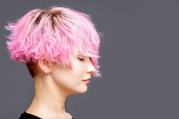 Woman with pink hairstyle stands with closed eyes side view on gray background with copy space. - Photo, Image