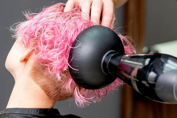 Hands of hairdresser dries pink hair of woman close-up. - Photo, Image