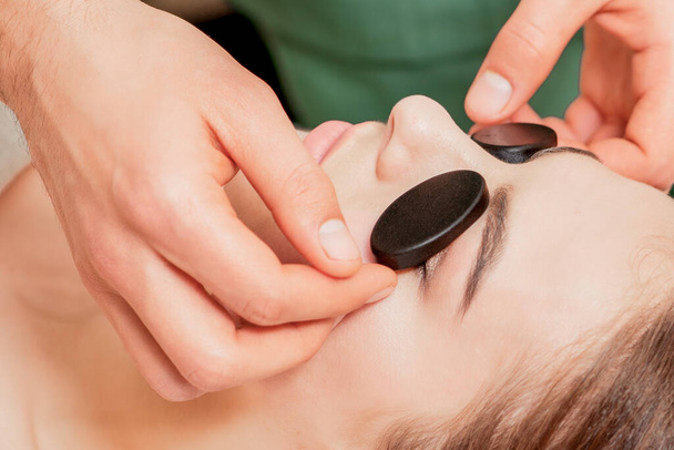 Mains de massothérapeute met des pierres de massage sur les yeux de la jeune femme pendant le massage relaxant
. - Photo, image