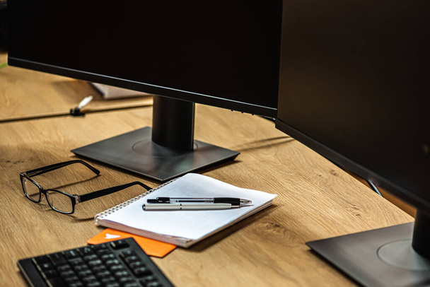 Desktopweergave, twee computerschermen, toetsenbord, muis en computer hebben een blanco zwart scherm op een houten bureau en een kantoorachtergrond - Foto, afbeelding