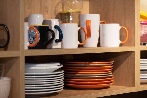 Dřevěná kuchyňská skříň s mnoha bílých a barevných a čisté keramické nádobí, talíře, všechny úhledně uklizené na policích moderních domácích interiérových skříní v obývacím pokoji - Fotografie, Obrázek