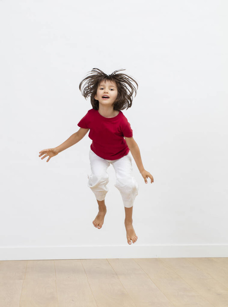 playful smiling child with hair all over enjoying jumping with joyful energy to express cheerful dynamism, fun sports and excitement over white background - Foto, afbeelding