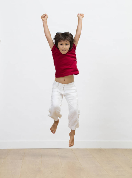 divertido y excitado niño saltando y levantando brazos para expresar felicidad, libertad, energía, motivación y alegría sobre fondo blanco
 - Foto, Imagen