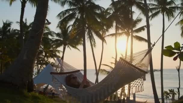Genç bir kadın tropik iklimde deniz kenarında hamakta dinleniyor. - Video, Çekim