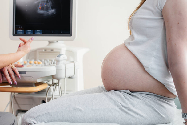 Μια έγκυος κοπέλα κάνει υπέρηχο της κοιλιάς της κλινικής σε κοντινό πλάνο. Ιατρική εξέταση - Φωτογραφία, εικόνα