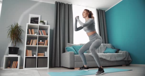 Active charming woman crouching while standing on yoga mat - Video, Çekim