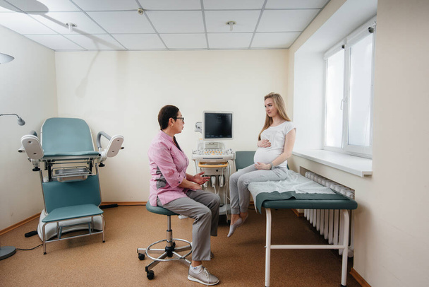 Μια έγκυος κοπέλα καθοδηγείται από γιατρό μετά από υπέρηχο στην κλινική. Ιατρική εξέταση - Φωτογραφία, εικόνα