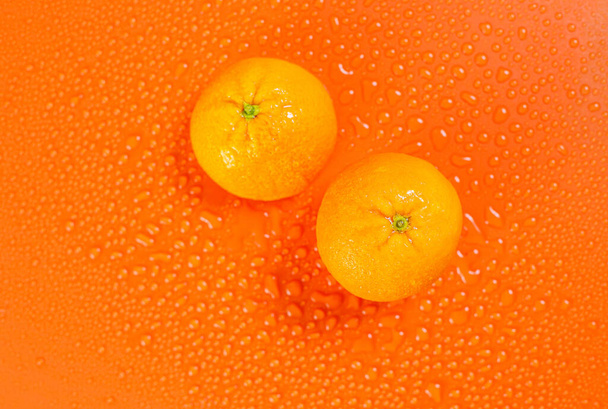 Duas laranjas inteiras em um fundo laranja com gotas de água
 - Foto, Imagem