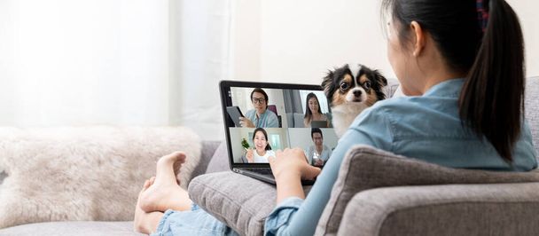 Banner ázsiai nő kanapén és csapat laptop képernyőn beszél és vita videokonferencia és a kutya megszakítás.Otthonról dolgozik, Távolról dolgozik, Háziállat megszakítás és önálló elszigetelés. - Fotó, kép