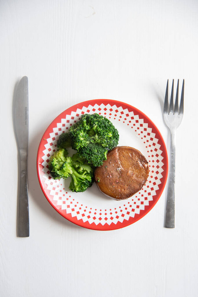 Seitan with broccoli also a knife and a fork in white table, vertical image - Photo, Image