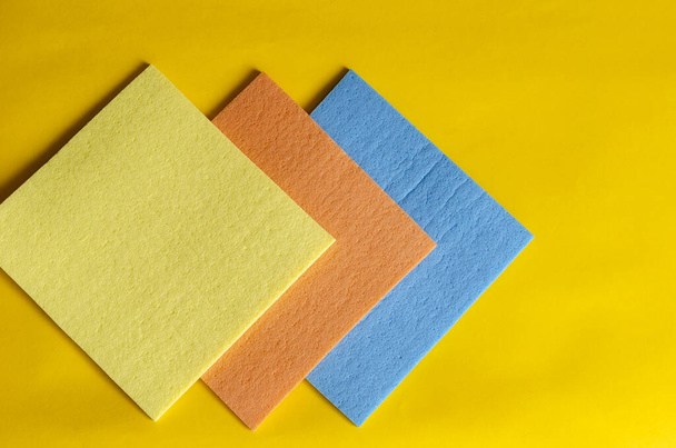 Kitchen napkins for cleaning on a yellow background. Geometric figure from kitchen napkins. Three multi-colored napkins for dishes. Home routine and commercial cleaning company. Selective focus. - Photo, Image
