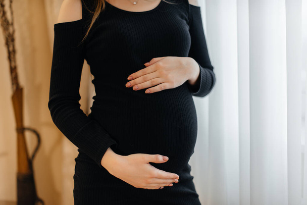 A pregnant girl touches her belly in the apartment in close-up - Foto, afbeelding