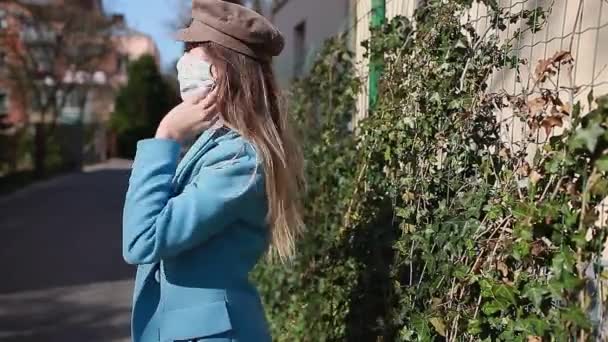 女性はコロナウイルスの流行の間に屋外で再利用可能な手作りのマスクを身に着けている。女の子だけで空の通りを歩く。安全だ。春のファッション - 映像、動画