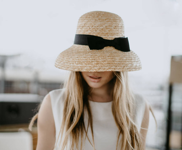 a straw hat almost completely covers the face of a beautiful girl in a white dress - Photo, Image