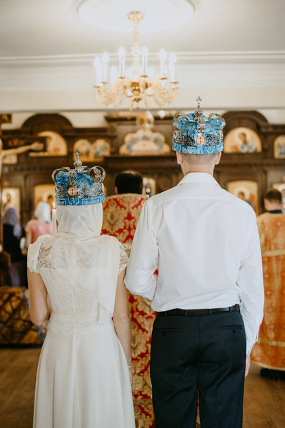 uma mulher e um homem realizam uma cerimônia de casamento em uma igreja em coroas de casamento vista das costas esposa e marido
 - Foto, Imagem