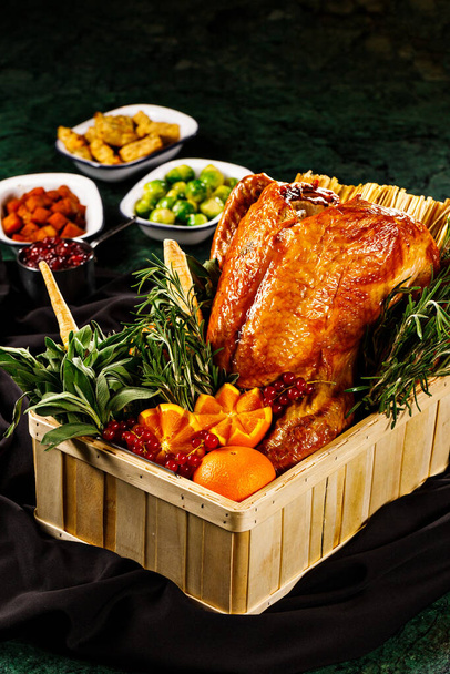 Roasted whole duck in a basket prepared with thymes, basil, mandarin and cranberry perfect for thanksgiving and special occasion. Vegetables side dishes in black background. - Photo, Image
