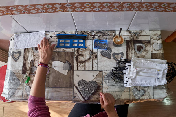 Manos de mujer cosiendo máscaras de tela en casa con una máquina de coser para proteger contra el coronavirus
. - Foto, Imagen