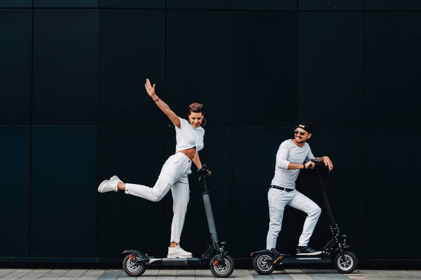 Una chica y un chico están caminando en scooters eléctricos por la ciudad, una pareja enamorada en scooters. - Foto, imagen