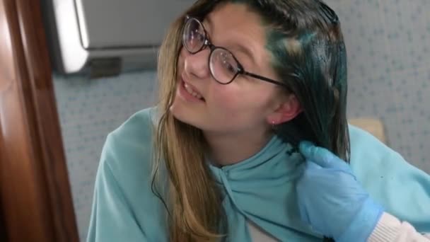 Egy Y-generációs lány kékre festi a szőke haját otthon a fürdőszobában. Házi szőrápolás a koronavírus karantén alatt. - Felvétel, videó