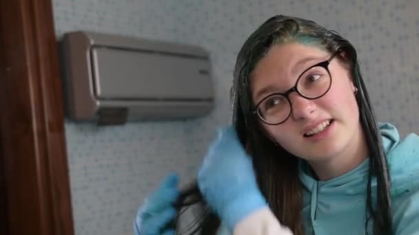Egy Y-generációs lány kékre festi a szőke haját otthon a fürdőszobában. Házi szőrápolás a koronavírus karantén alatt. - Felvétel, videó