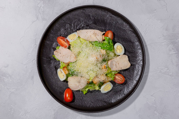 Caesar salad with chicken breast on a dark plate. Home-made chicken fillet, cherry tomatoes, Parmesan cheese, quail eggs, crackers and sauce. European cuisine. Dish from a restaurant or cafe menu. Top - Foto, imagen