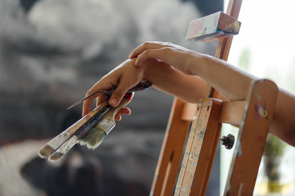 Taiteilijan käsi siveltimillä hämäräperäiseen maalaukseen
 - Valokuva, kuva
