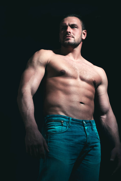 Strongand serious muscular man. Handsome sexual strong man with muscular body in jeans posing in studio on black background. - Фото, зображення