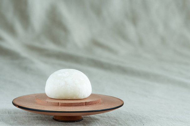 Close-up em um mochi daifuku branco brilhante em uma placa de madeira em um tecido verde cáqui. Conceito para sobremesa e comida asiática, cultura e tradições japonesas, viagens e celebrações, pausa para chá e café
 - Foto, Imagem